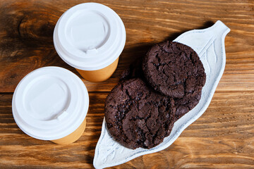 Two glasses takeaway coffee and an American cookie on dark background.