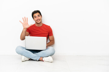 Caucasian handsome man with a laptop sitting on the floor counting five with fingers