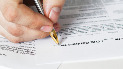 A businessman sitting at an office desk signs a contract with a shallow emphasis on signing....