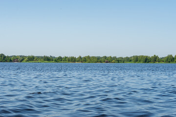 Summer landscape with blue skies and blue wavy water of a forest lake. In the middle of a warm, sunny summer with fresh green foliage. Harmony in nature