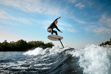 athletic man balancing on foilboard on wave on sunny day