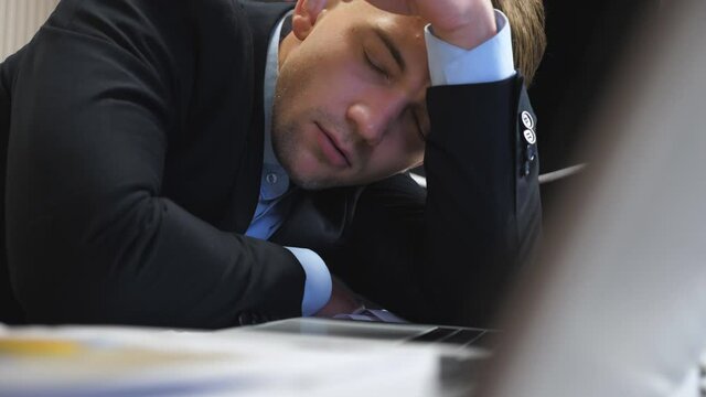 Dolly shot to tired boss in formal suit falling asleep on table at boardroom. Exhausted manager sleeping on table with laptops at office. Young entrepreneur napping at workplace. Close up Slow motion