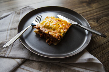 A piece of delicious hot lasagna with red wine. Traditional Italian lasagna. Part. Italian food. Food on a black plate. Bolognese sauce. Bechamel sauce. Still life of food.