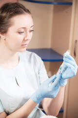 A young doctor Caucasian woman in medical clothes and rubber gloves without a protective mask is drawing a vaccine or medicine from an ampoule into a syringe. Failure to comply with medical safety