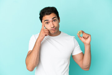 Young man holding a Bitcoin over isolated blue background thinking an idea