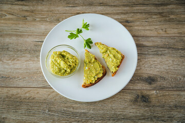 Avocado toasts with egg and shrimp on white plate on wooden table background
closeup.