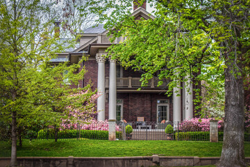 Side of historical old home with ornate pillars and balconies in springtime with pink flowering...