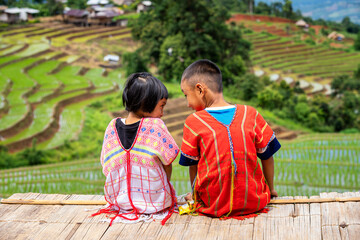 A boy and a girl dressed in hill tribe clothing are sitting on the terraced rice fields. A Hmong farmer looking at the terraced rice fields.