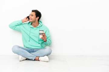 Caucasian handsome man sitting on the floor holding coffee to take away and a mobile