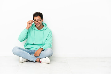 Caucasian handsome man sitting on the floor with glasses and surprised