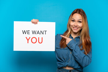 Naklejka premium Teenager girl over isolated blue background holding We Want You board and pointing it