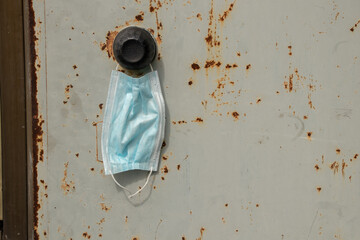 a medical mask hangs on the handle on an old iron rusty door on the street at the house, quarantined