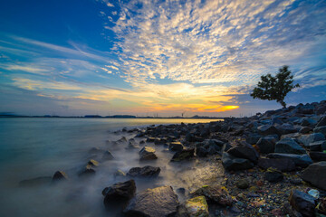 Naklejka premium Enjoying the sunset on the marina beach with houses on stilts and rocks in the background