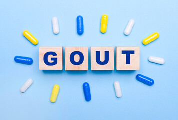 On a light blue background, multicolored pills and wooden cubes with the text GOUT. Medical concept