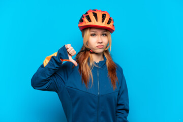 Young cyclist girl isolated on blue background showing thumb down with negative expression