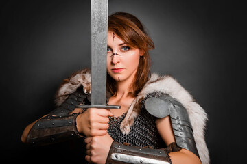 Medieval woman warrior in chain mail armor and polar fox fur on her shoulders standing with a sword...