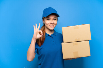 Delivery girl over isolated blue wall showing ok sign with fingers