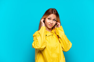 Teenager girl wearing a rainproof coat over isolated blue background frustrated and covering ears