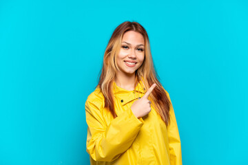 Teenager girl wearing a rainproof coat over isolated blue background pointing to the side to present a product