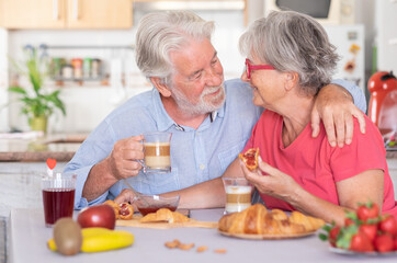 Beautiful elderly couple smiling having breakfast at home. Senior people relaxed and happy