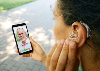 Adult woman with a hearing aid in her ear communicates with her father via video communication via...