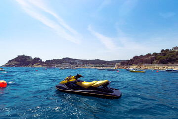 Fototapeta premium Fantastic shot of a wavy sea with a jet ski in front and many floating boats on mountains background of Tossa de Mar