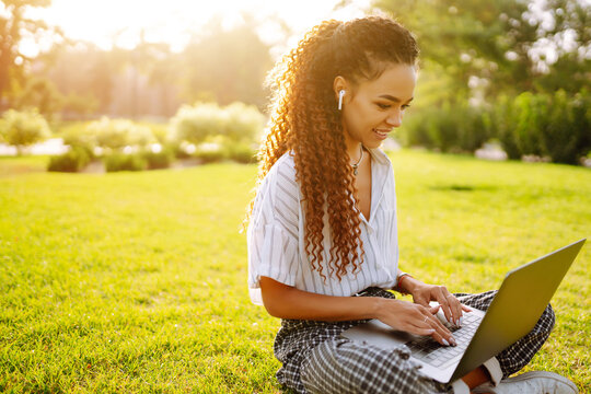 Freelancer woman using laptop computer sitting on grass at park. Young woman working online or studying and learning while using notebook. 