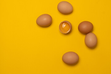 Organic brown chicken eggs and one broken egg with yolk on a yellow background