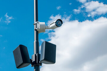 A CCTV camera is mounted on a pillar with a blue sky and clouds in the background.