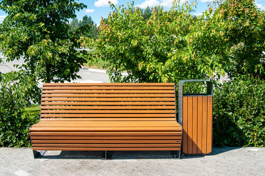 Wooden bench with wooden trash can in a park with green spaces on a summer day, nobody.