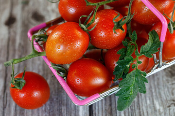 A shopping basket filled with cherry tomatoes on a wooden background.