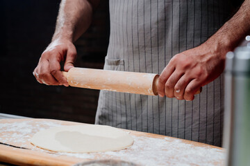 hands roll the dough into a thin layer. Cooking pizza, noodles or pitta at home