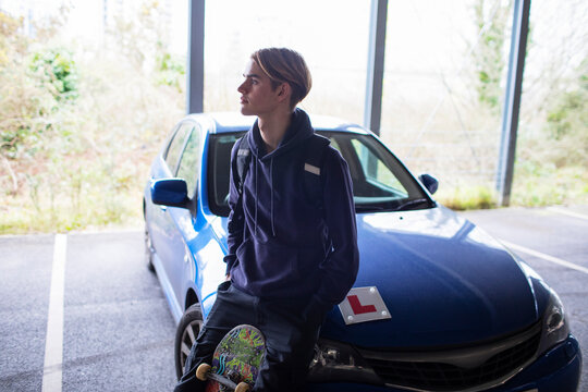 Teenage boy with skateboard on car with learner permit in car park