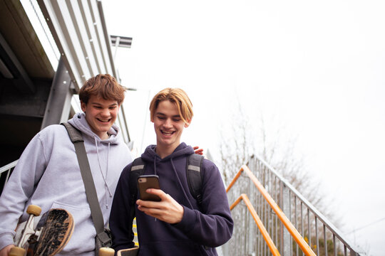 Happy teenage boys using smart phone on steps