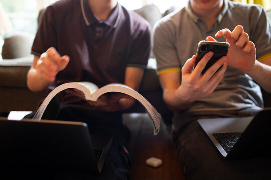 Teenage boys with textbook and smart phone studying at home