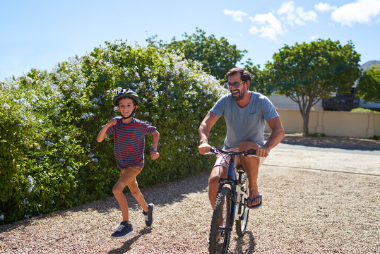 Happy father and son running and riding bike in sunny driveway