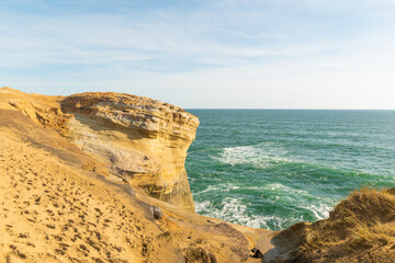 Rocky ocean coast. Yellow sandy cliffs rise above the turquoise waters. Light foam waves. The sky is light blue with light clouds. There is an empty space for your insert.