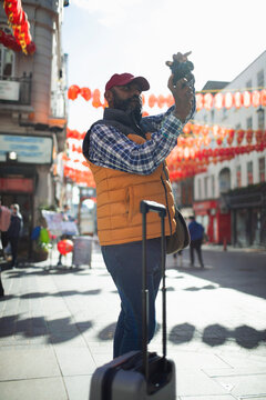 Male tourist with suitcase using digital camera in sunny Chinatown