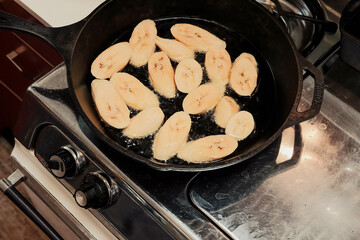 Caribbean maduros frying in oil in a cast iron pan on stove