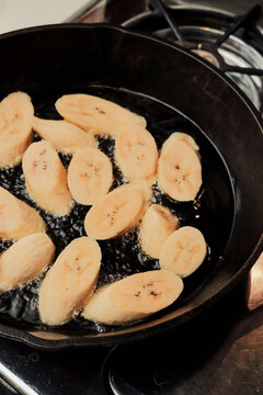 Sliced sweet plantains frying in oil in cast iron pan