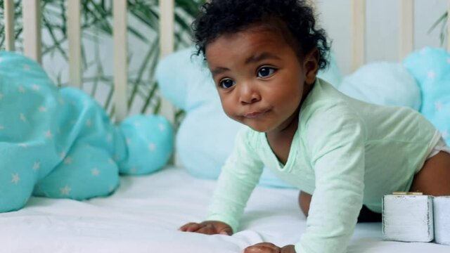 baby boy African American sits on the bed on a blue cotton bed and wants to crawl
