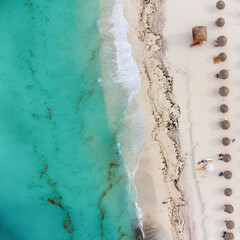 Sea beach. White sand and turquoise ocean water. Clear sunny day. Thatched beach umbrellas are placed along the shore. View from above. Aerial photography.There is no one in the photo.