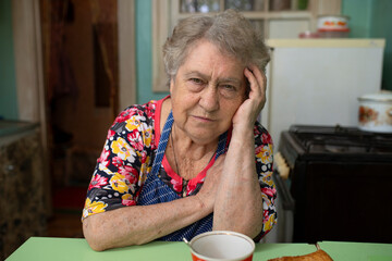 Sad old woman sitting at the kitchen table at home.