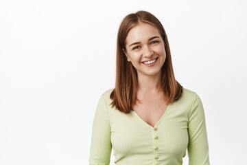 Fototapeta premium Close up of young pleasant girl, smiling and looking friendly, happy cute face expression, smile white teeth, standing in casual blouse against white background