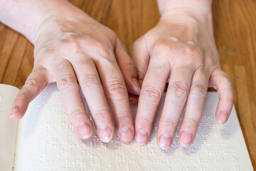 front view of female fingers reading book with braille closeup on wooded table