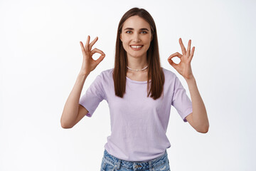 Image of smiling young woman shows okay OK signs, zero problems, recommend something good, positive feedback, likes and agrees, approve, standing over white background