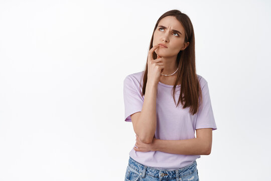 Hmm let me think. Young woman looks up thoughtful, touch lip and thinking, making choice, deciding what to order takeaway, standing against white background