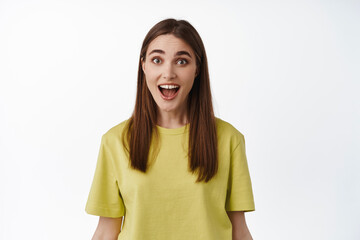 Really amazing. Surprised brunette girl drop jaw, gasping excited, checking out smth awesome, looking with happy and astonished face, standing against white background