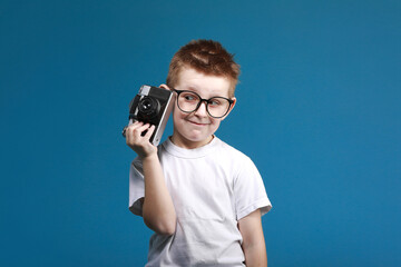 Little boy taking a picture using a retro camera. Child boy with vintage photo camera isolated on blue background. Old technology concept with copy space. Child learning photography .