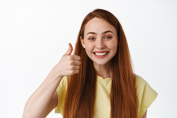 Close up of excited redhead girl says yes, shows thumbs up in approval, compliment good choice,...